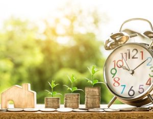 zegarek drewniany domek i stosiki monet